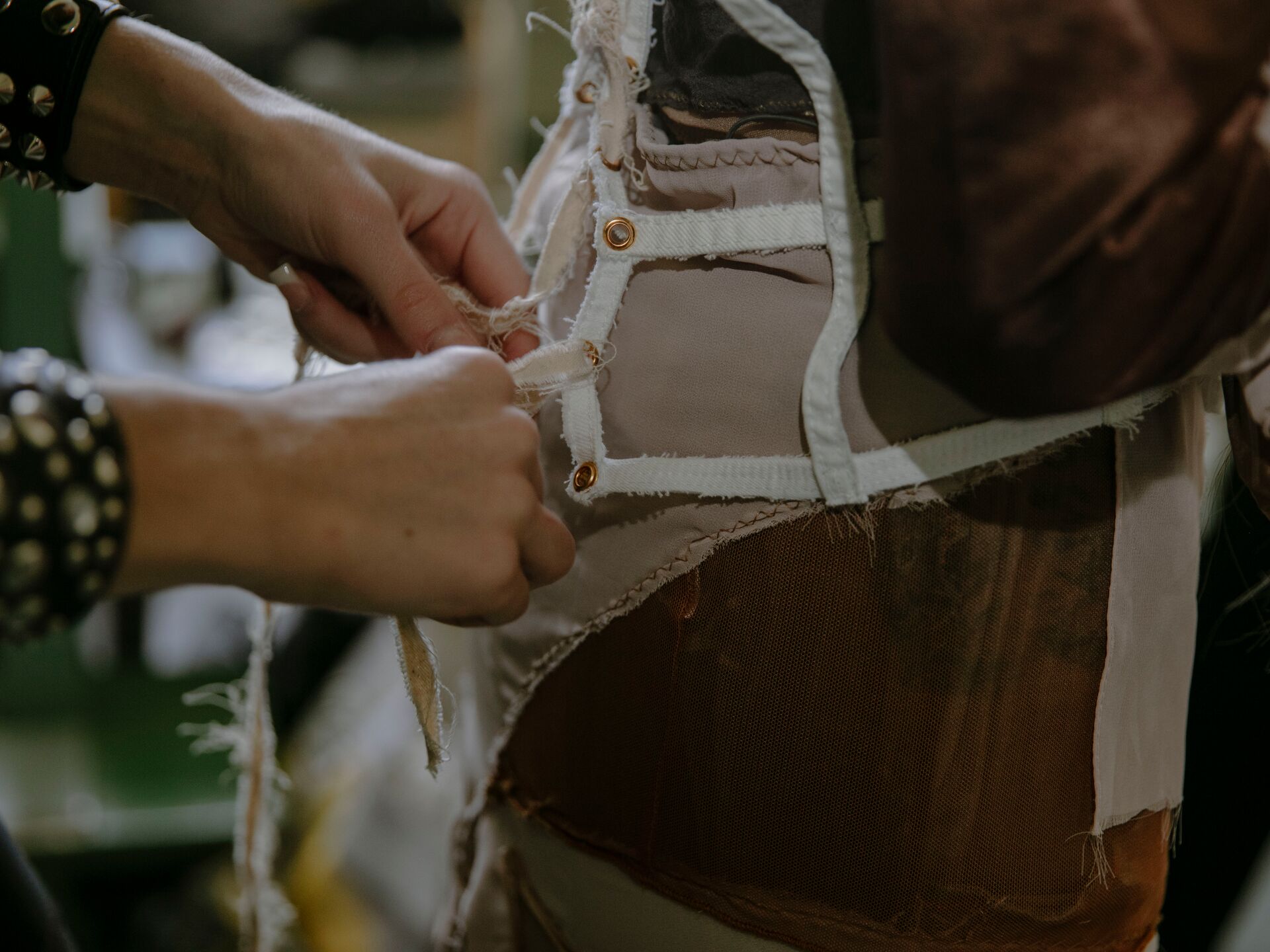 Nahaufnahme von Händen, die an einem Kleidungsstück arbeiten – Stoff wird festgehalten oder genäht, sichtbare Nähte, Knopflöcher und verschiedene Materialien.