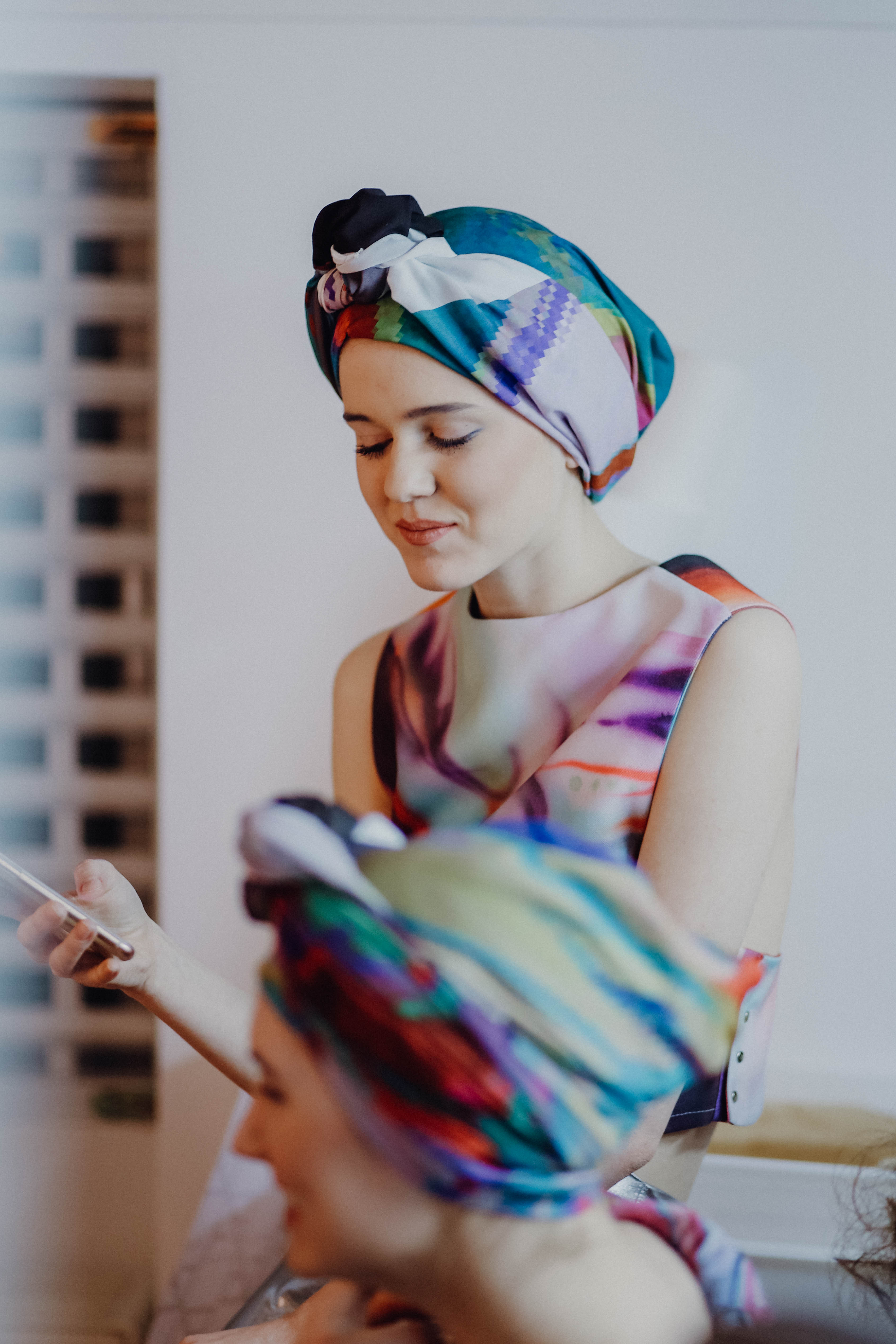 Zwei Frauen mit bunten Kopftüchern und farbenfroher Kleidung, eine blickt auf ein Smartphone.